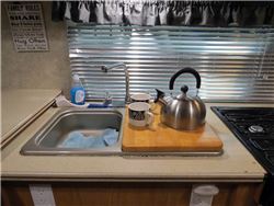 RV kitchen sink, with sink cover cutting board covering half the sink, a tea kettle a coffee mug sitting atop.