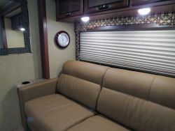 RV living room with a tan fold out couch, mirror on the wall, and under cabinet lighting.
