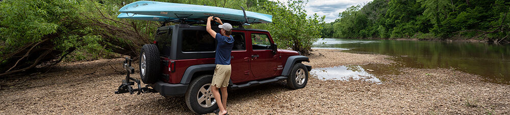 man hooking up kayaks on Jeep roof rack watersport carrier.