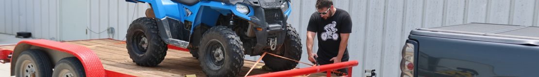 Man hooking up atv to red trailer. 