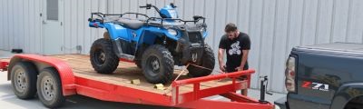 Man hooking up atv to red trailer. 