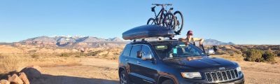 woman standing next to suv with bike on roof rack. 