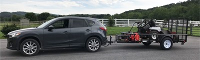 grey suv pulling landscape trailer hauling lawnmower.