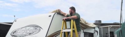 man on ladder putting cover over roof of rv. 