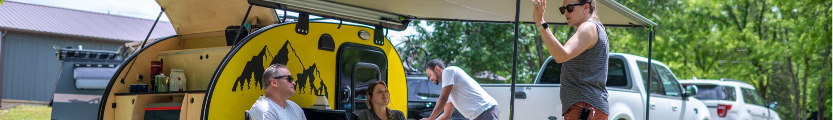 woman and men relaxing outside yellow teardrop camper.