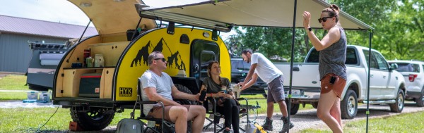 woman and men relaxing outside yellow teardrop camper.