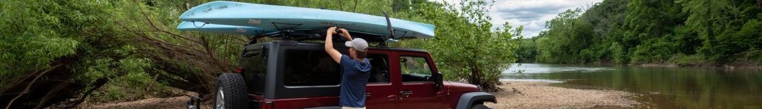 A person putting kayaks on roof of a red jeep. 