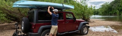 A person putting kayaks on roof of a red jeep. 